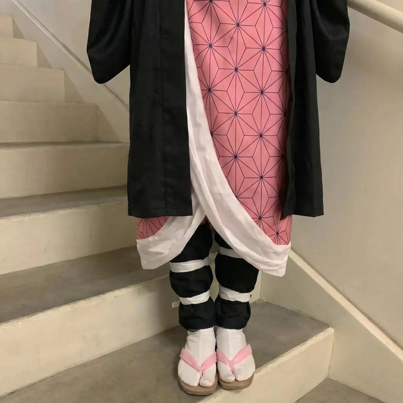 Puede incluir: Un atuendo de cosplay con un kimono rosa con estampado geom&eacute;trico, pantalones negros y calcetines blancos con correas rosas. El atuendo incluye una chaqueta negra y sandalias de madera. El disfraz se usa en una escalera.