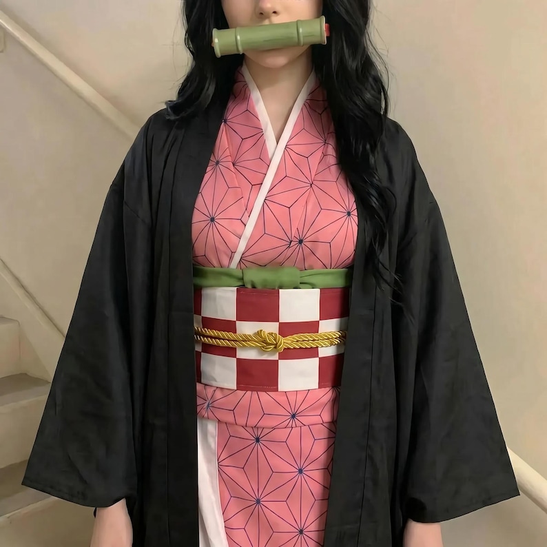 Puede incluir: Un kimono rosa con un patr&oacute;n geom&eacute;trico, un cuello blanco y un obi a cuadros rojos y blancos. El atuendo incluye un haori negro y un bozal de bamb&uacute; verde. Este atuendo de cosplay est&aacute; inspirado en un personaje de anime popular.