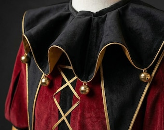 May include: A close-up of a jester costume. The costume features a black velvet collar with gold trim and small gold bells. The bodice is red velvet with gold crisscross lacing. The sleeves are red with a yellow diamond accent.