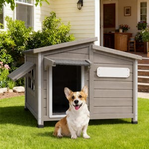 Puede incluir: Una caseta para perros de madera gris con molduras blancas y un pequeño toldo. Un perro corgi con pelaje marrón y blanco está sentado frente a la caseta sobre un césped verde. La caseta tiene un letrero blanco en blanco.