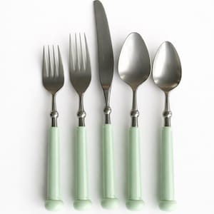 May include: A set of five pieces of silverware: two forks, a knife, and two spoons. The handles are a light green color, and the metal parts are silver. The silverware is arranged on a white background.