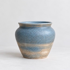 May include: A ceramic planter featuring a blue crackle glaze finish on the upper portion and a natural tan, ribbed texture on the lower section. The vessel has a wide, rounded body with a flared rim and a consistent, smooth circular opening.