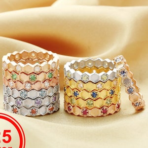 May include: Stack of silver, rose gold, and gold rings with a honeycomb design and colorful gemstones. The rings are on a beige fabric background. 925 Silver.