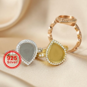 May include: Three rings with teardrop-shaped settings. One ring is silver with a gray setting and a halo of small clear stones. The second ring is gold with a gold setting and a halo of small clear stones. The third ring is gold with a square setting.