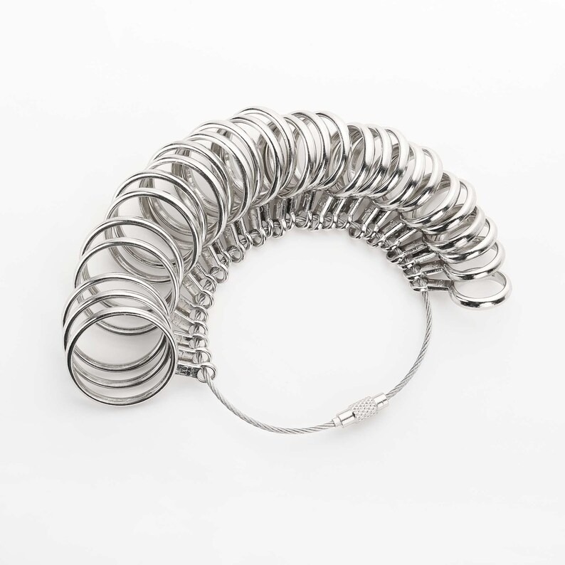 May include: A silver ring sizer with a series of connected rings of different sizes. The rings are attached to a silver cable with a clasp.