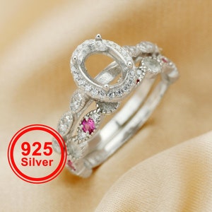 May include: A silver ring set with a large oval-shaped setting surrounded by smaller clear stones. The band is decorated with smaller clear stones and pink stones.