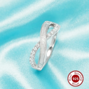 May include: A silver infinity ring with a brushed finish and small clear cubic zirconia stones. The ring is on a light blue background. Real Sterling 925 Silver.