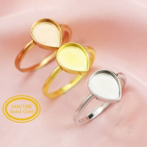 Könnte beinhalten: Drei tropfenförmige Ringe mit einer Zargenfassung für einen Stein. Die Ringe sind aus 14k/18k massivem Gold gefertigt und in Gelb-, Weiß- und Roségold erhältlich.