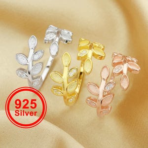 May include: Three leaf-shaped rings in silver, gold, and rose gold. The silver ring is stamped with "925 Silver". The rings have a delicate design with small, oval-shaped leaves. The gold and rose gold rings have small, clear stones.