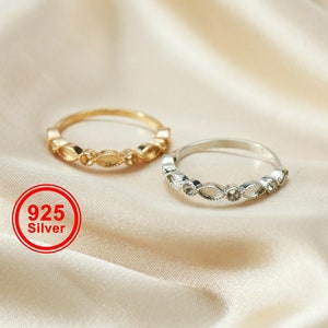 May include: Two delicate rings, one gold-toned and one silver-toned, are displayed. Each ring features a repeating pattern of oval-shaped designs. The rings are set against a soft, neutral background. A red circle with the text "925 Silver" is visible.