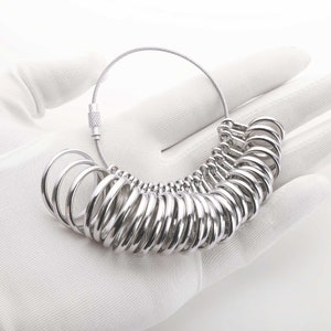 May include: A silver ring sizer with a chain and clasp. The sizer has a series of rings of different sizes.