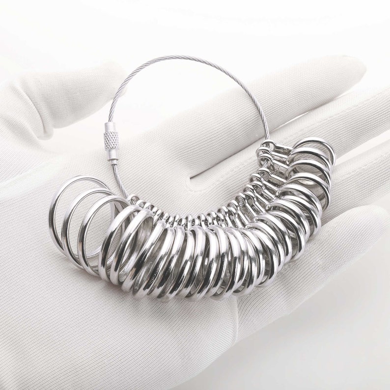 May include: A silver ring sizer with a chain and clasp. The sizer has a series of rings of different sizes.