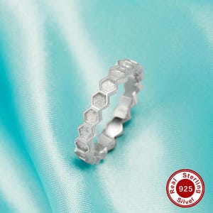 May include: A silver ring with a honeycomb design. The ring is made of sterling silver and has a textured finish. The ring is on a light blue background. Real Sterling 925 Silver.