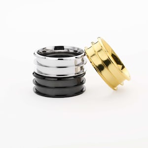 May include: Three metal rings stacked on top of each other. The top ring is gold, the middle ring is silver, and the bottom ring is black.