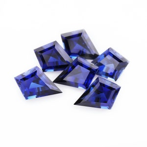 May include: A group of six blue sapphire gemstones, each cut into a kite shape with a pointed tip. The gemstones are arranged in a cluster on a white background.