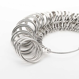 May include: A silver ring sizer with a chain and a clasp. The sizer has a series of rings of different sizes, each connected to the next by a small chain link. The sizer is a useful tool for determining the correct ring size.