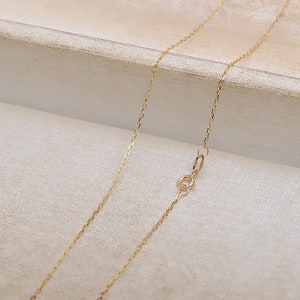May include: A gold chain necklace with a lobster clasp closure. The chain is made of a delicate, fine-link design.