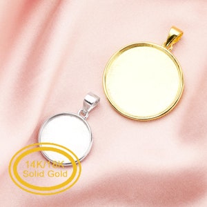 May include: Two round pendant settings, one gold and one silver, on a pink fabric background. The gold pendant setting has a 14k/18k solid gold label.