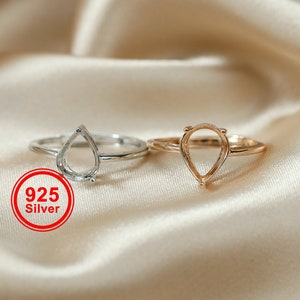 May include: Two rings with teardrop-shaped settings. The ring on the left is silver and the ring on the right is gold.