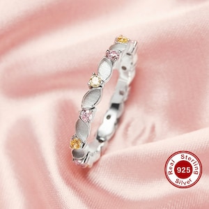 Può includere: Un anello d'argento con un design delicato che presenta piccole pietre preziose rosa, gialle e bianche. L'anello è realizzato in argento sterling 925.