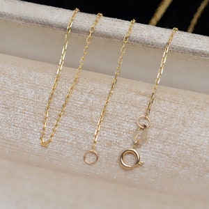 May include: Two gold chains with lobster claw clasps. The chains are on a white surface.