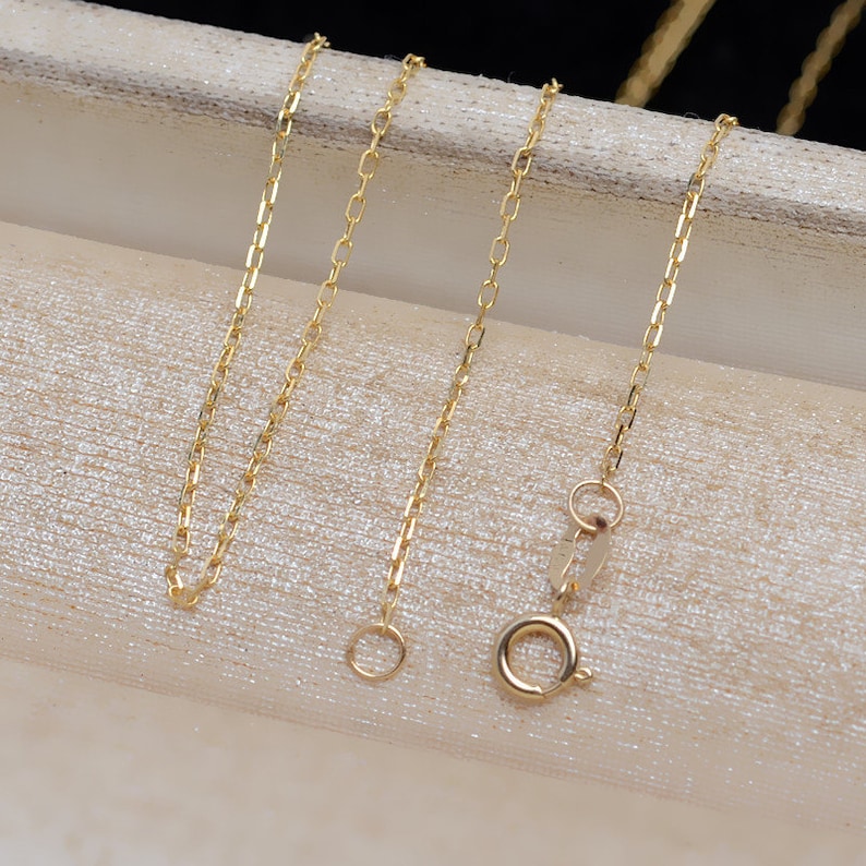 May include: Two gold chains with lobster claw clasps. The chains are on a white surface.