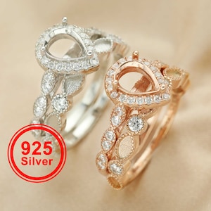 May include: Two pear-shaped rings with a clear stone setting. The ring on the left is silver with a delicate leaf design. The ring on the right is rose gold with a similar leaf design. Both rings are adorned with small clear stones.