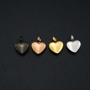 May include: Four heart-shaped pendants in different metal finishes: black, rose gold, gold, and silver. Each pendant has a loop at the top for attaching to a chain.
