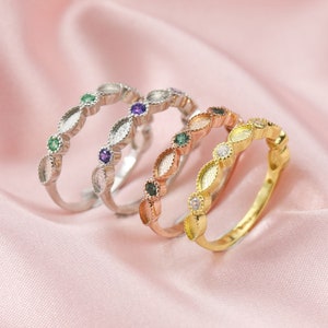 Könnte beinhalten: Drei zarte Ringe mit ovalen Fassungen. Die Ringe sind silber, roségold und gold. Jeder Ring hat eine Reihe kleiner Edelsteine in der Mitte. Die Edelsteine sind grün, lila und klar.