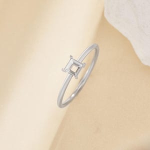 May include: A silver ring with a square setting for a gemstone. The ring is simple and elegant.