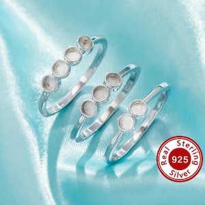 Pode incluir: Três anéis de prata esterlina com várias configurações de moldura. Os anéis são exibidos em uma superfície de cetim azul claro. Cada anel tem um número diferente de configurações de moldura, variando de dois a cinco. Um selo vermelho e branco "Real Sterling 925 Silver" está no canto inferior direito.