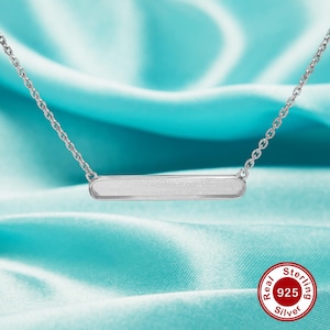 May include: A silver bar necklace with a brushed finish. The necklace is on a light blue background with a red and white label that says "Real Sterling 925 Silver".