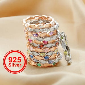 May include: A stack of sterling silver rings with colorful gemstones. The rings feature a repeating oval design with alternating silver and rose gold bands. The image includes a red circle with the text "925 Silver".