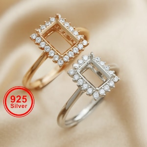 Puede incluir: Dos anillos de plata con un engaste cuadrado para una piedra preciosa. Los anillos están adornados con pequeñas piedras transparentes alrededor del engaste. El anillo de la izquierda es de color dorado, mientras que el anillo de la derecha es de color plateado. El texto "925 Silver" es visible en rojo sobre un círculo blanco.