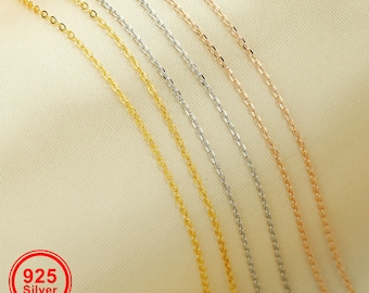 May include: Five different chain necklaces in gold, silver, and rose gold. The chains are laid out in a row on a cream-coloured fabric background. The text "925 Silver" is visible in a red circle.