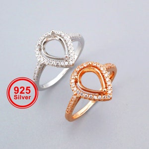 May include: Two pear-shaped rings with a clear stone setting. The ring on the left is silver and the ring on the right is gold.