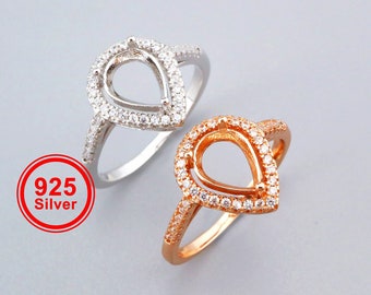 May include: Two pear-shaped rings with a clear stone setting. The ring on the left is silver and the ring on the right is gold.