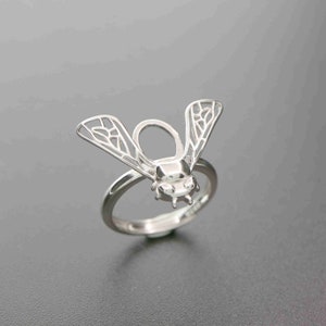 Könnte beinhalten: Silberring mit einem detaillierten Bienendesign. Die Flügel der Biene sind geöffnet und der Körper ist massiv. Der Ring ist aus Silber und hat eine polierte Oberfläche.