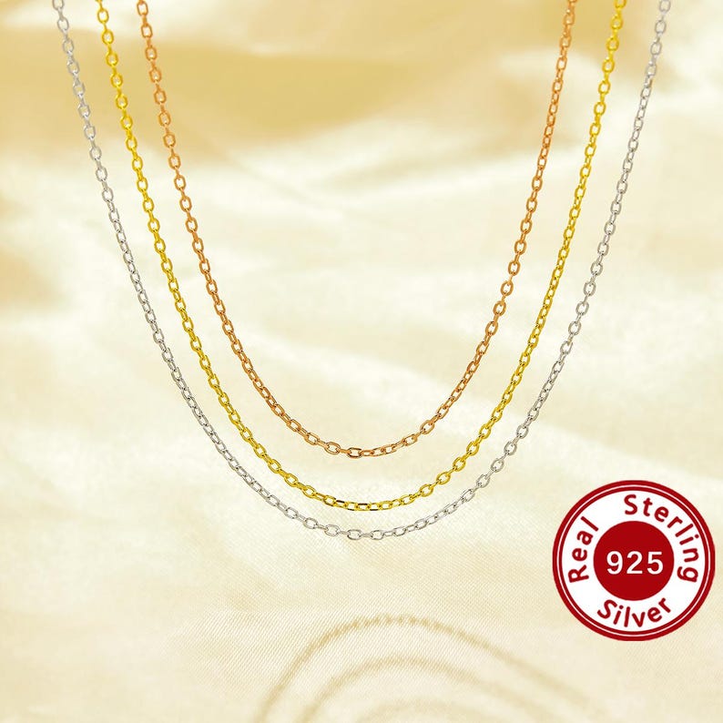 May include: Three silver chains, one gold chain, and one rose gold chain layered on a cream-colored background. The chains are all the same style, with small, oval links. A red circle with the text "Real 925 Sterling Silver" is in the lower right corner.