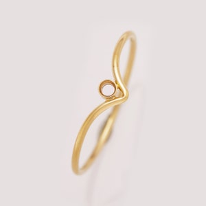 Könnte beinhalten: Ein goldener Ring mit einem einfachen, geschwungenen Design. Der Ring hat eine kleine, runde Öffnung in der Mitte.