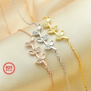 May include: Three delicate silver, gold, and rose gold bracelets with a leaf design and small clear stones. The bracelets are on a light beige background.