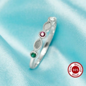 May include: A silver ring with three small gemstones. The ring has a textured design and features a red, green, and white gemstone. The ring is labeled "Real Sterling 925 Silver".