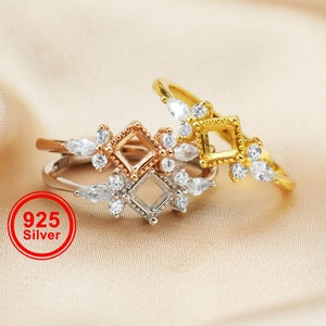 May include: Three silver rings with a square setting and clear stones. The rings are stacked on top of each other. The top ring is gold, the middle ring is rose gold, and the bottom ring is silver. The rings are on a light brown fabric background. 925 Silver.