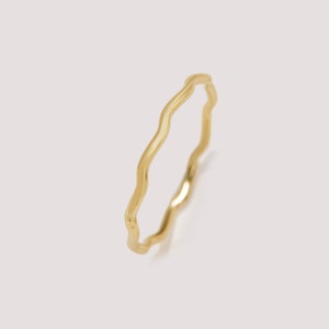 May include: A delicate, gold-colored ring with a wavy, organic design. The ring's surface reflects light, highlighting its smooth texture. The ring is a minimalist piece of jewelry.