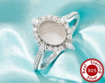 Op de afbeelding: Een zilveren ring met een ovale zetting, omringd door kleine, ronde en marquise-vormige heldere stenen. De ringband is ook versierd met kleine, heldere stenen. Een rode en witte ronde sticker met de tekst "Real Sterling 925 Silver" is zichtbaar.
