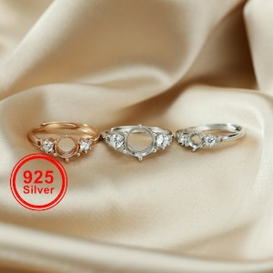 Puede incluir: Tres anillos de plata con piedras transparentes. Los anillos están sobre un fondo de tela beige. El anillo de la izquierda es de oro rosa. El anillo del medio es de plata. El anillo de la derecha es de plata. El texto "925 Silver" está en rojo sobre un círculo blanco.