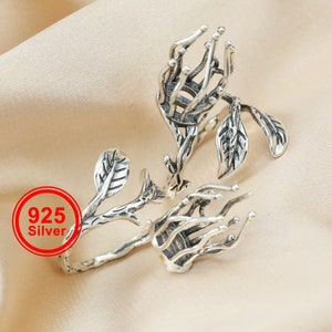 May include: A silver ring with a delicate branch design featuring leaves and a unique, intricate, openwork center. The ring is made of 925 silver.