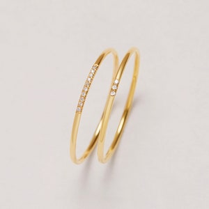 May include: Two gold rings with a row of small diamonds on one ring. The rings are stacked on top of each other.