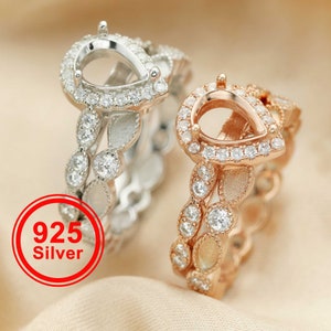 May include: Two pear-shaped rings with a delicate leaf design. The ring on the left is silver with clear stones, and the ring on the right is rose gold with clear stones. The rings are on a beige fabric background. 925 Silver.