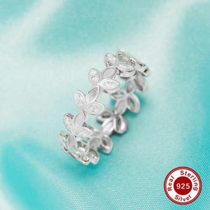 May include: A silver ring with a delicate design of leaves and small clear stones. The ring is made of sterling silver and is marked with "Real 925 Silver Sterling".